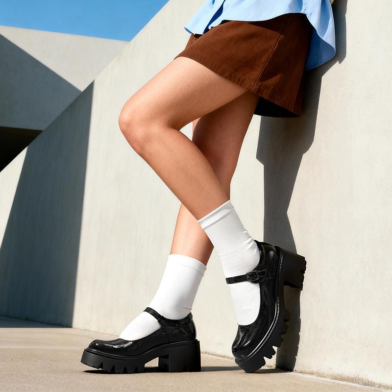 Glossy black platform Mary Janes styled with white socks and a brown skirt